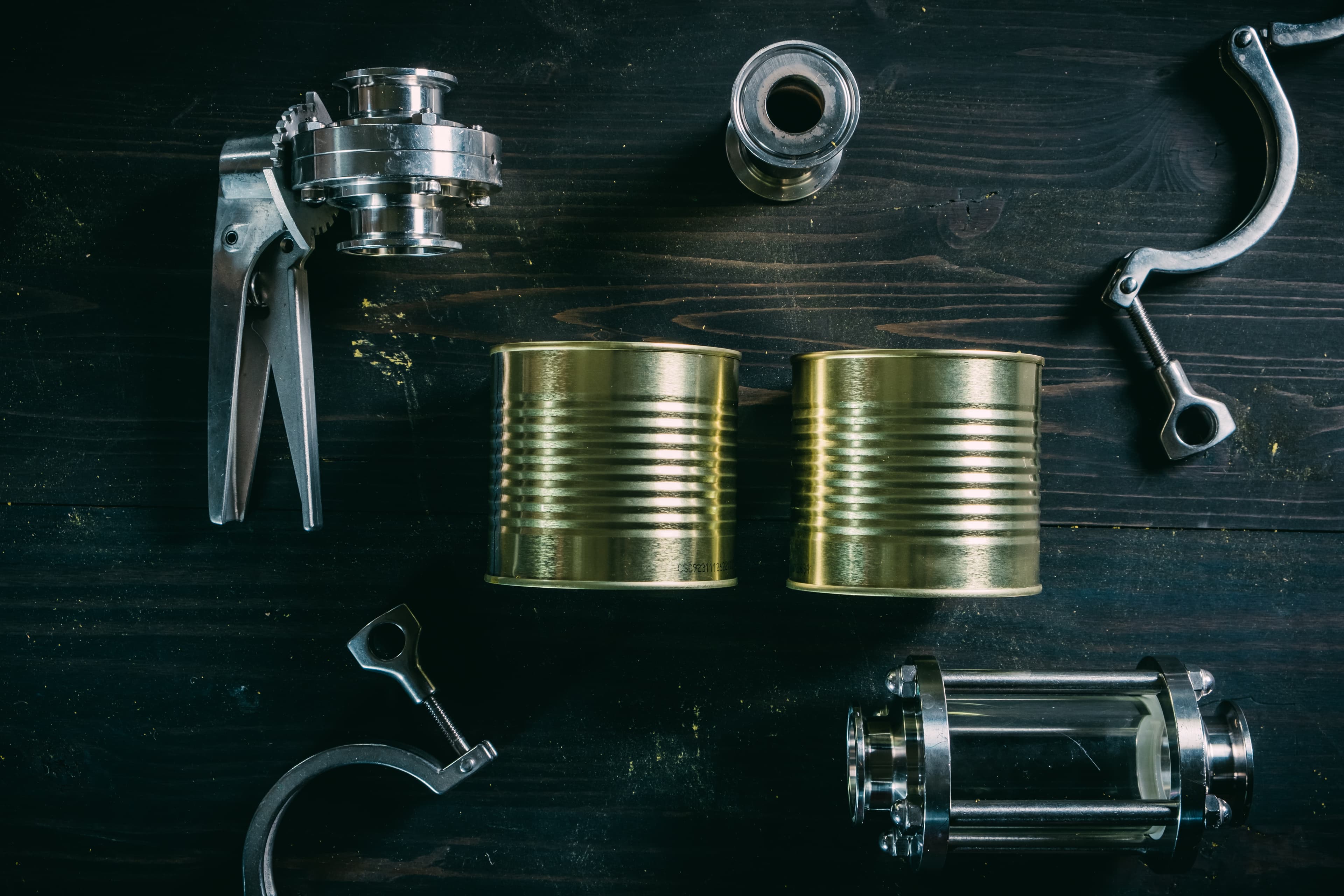 Two cylinder aluminum cans and a metal tool on a black wooden table