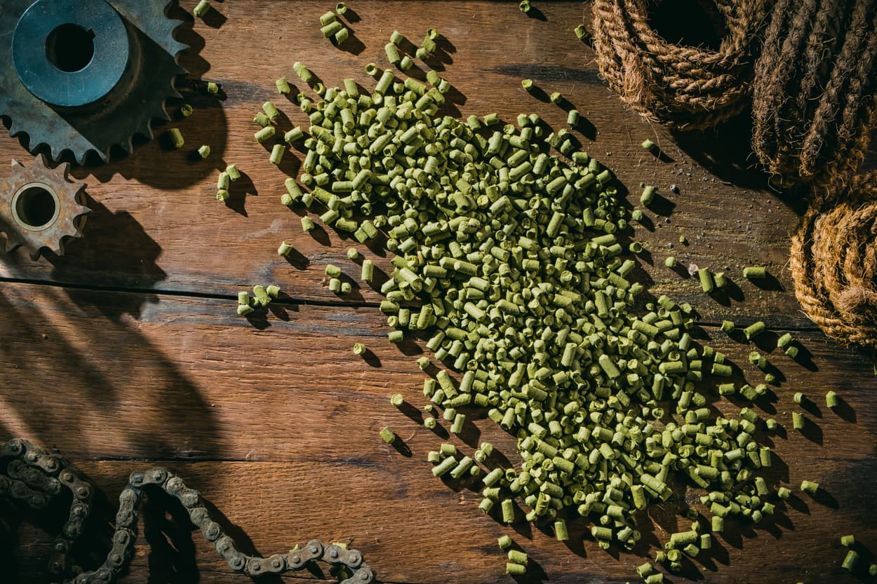 Aerial view of American Noble Hops pellets in a pile on wooden table top with rustic mechanical gear, farm equipment and burlap scattered around it